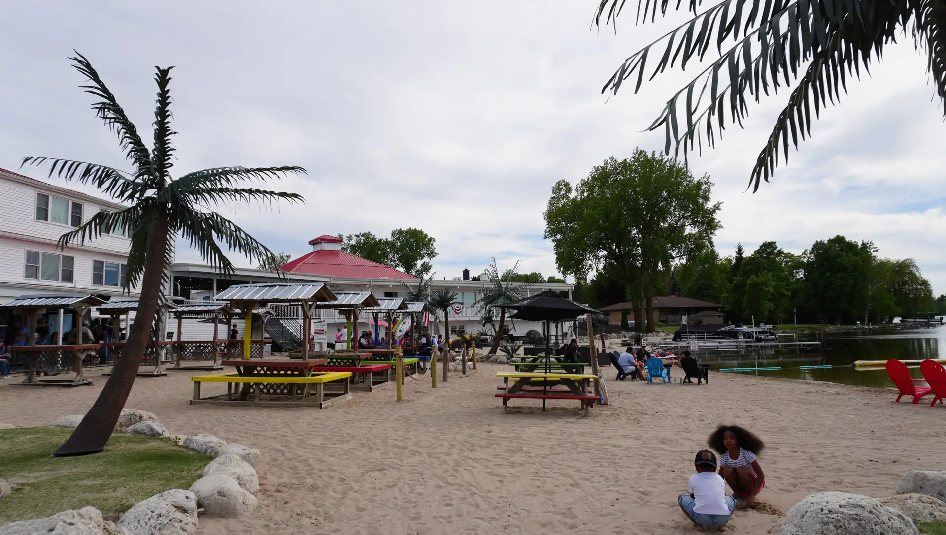 The beach with palms, picnic tables, and tiki huts on a summer afternoon